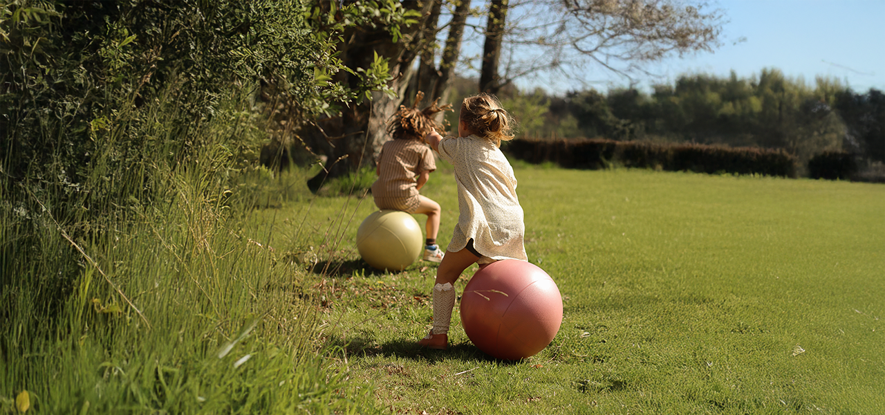 Two children playing on bouncy balls from Find That Hippo in a sunny green field