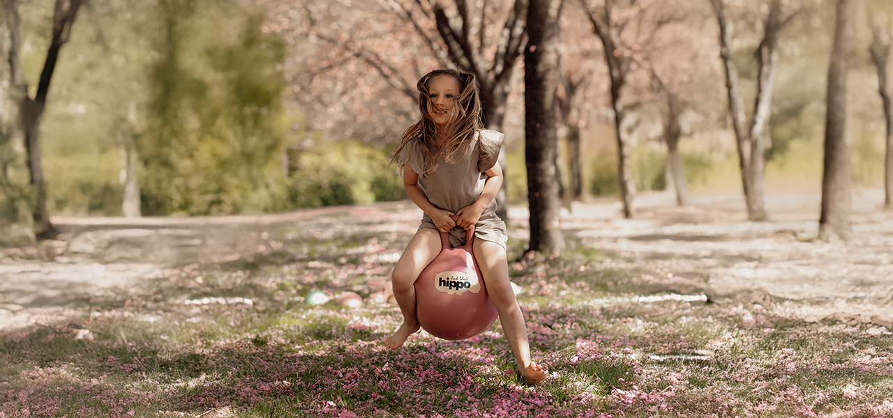 Girl bouncing on a pink bouncy ball from Find That Hippo in a spring landscape