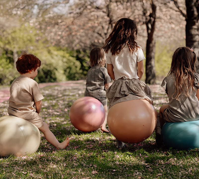 Group of children sitting on colorful bouncy balls from Find That Hippo in a spring park setting