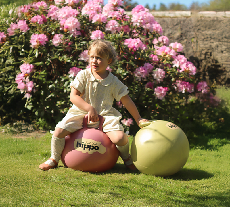 Girl sitting on two bouncy balls from Find That Hippo in a sunny garden with blooming flowers