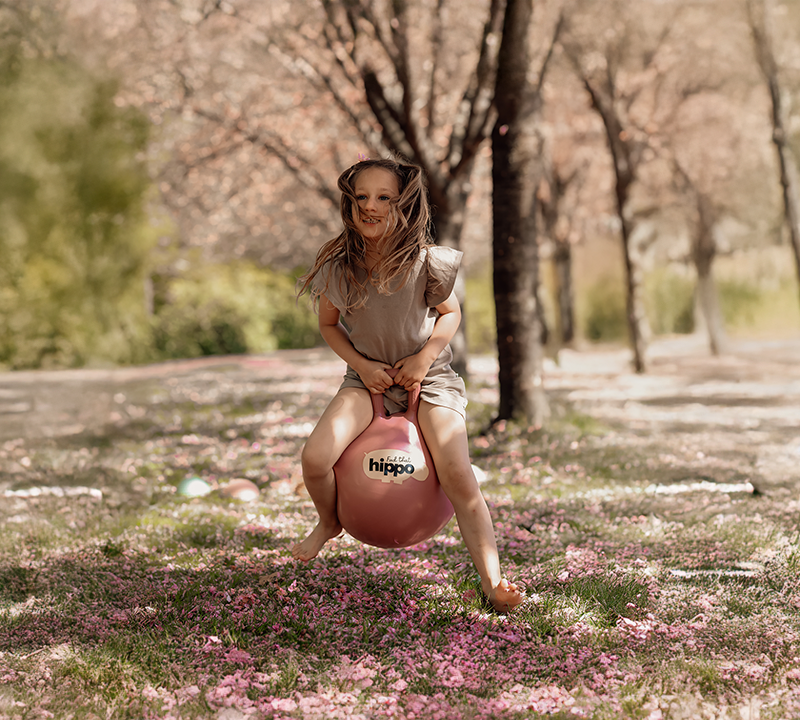 Girl bouncing on a pink bouncy ball from Find That Hippo in a spring landscape
