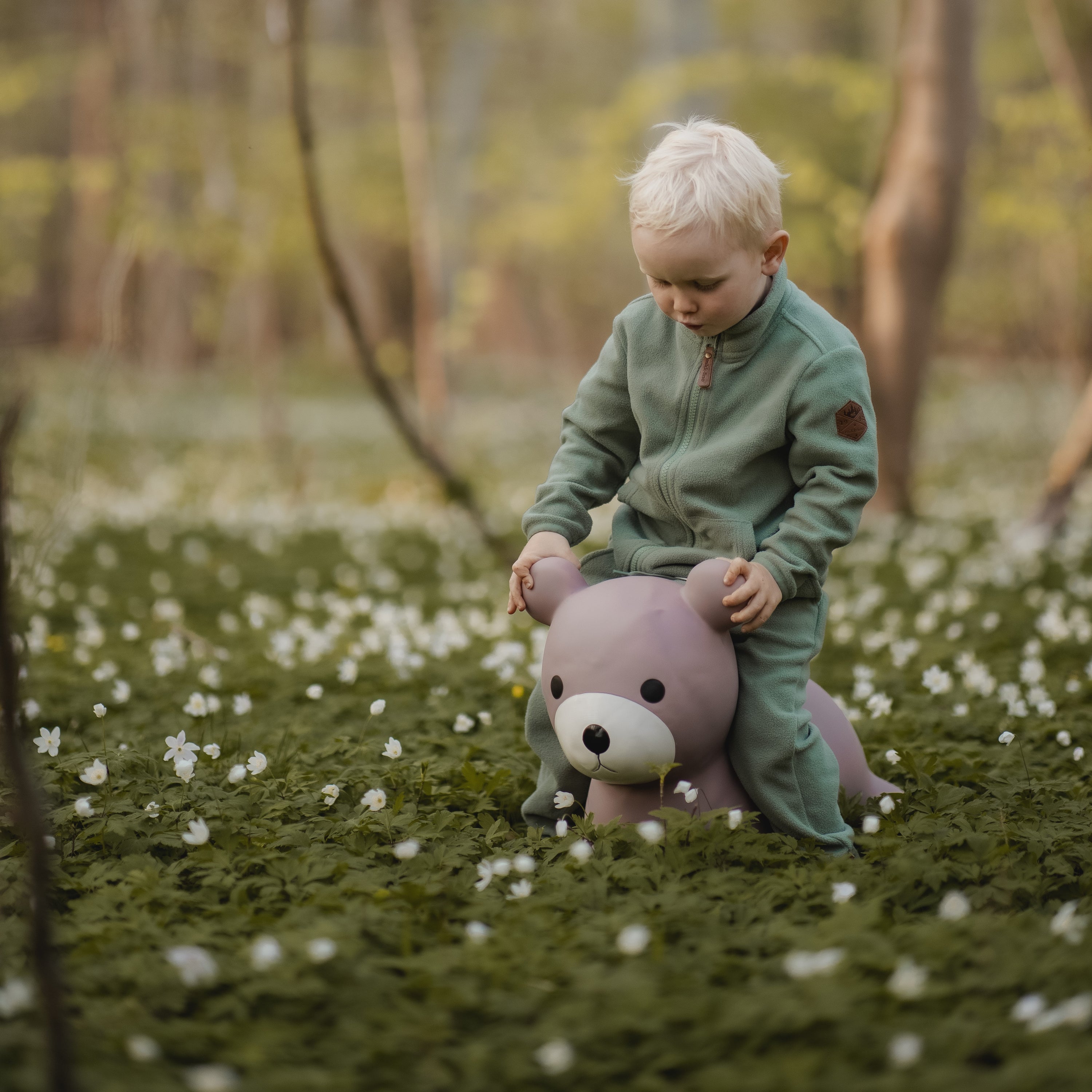Child sitting on Maya the bouncing bear toy in a blooming flower field – Find That Hippo