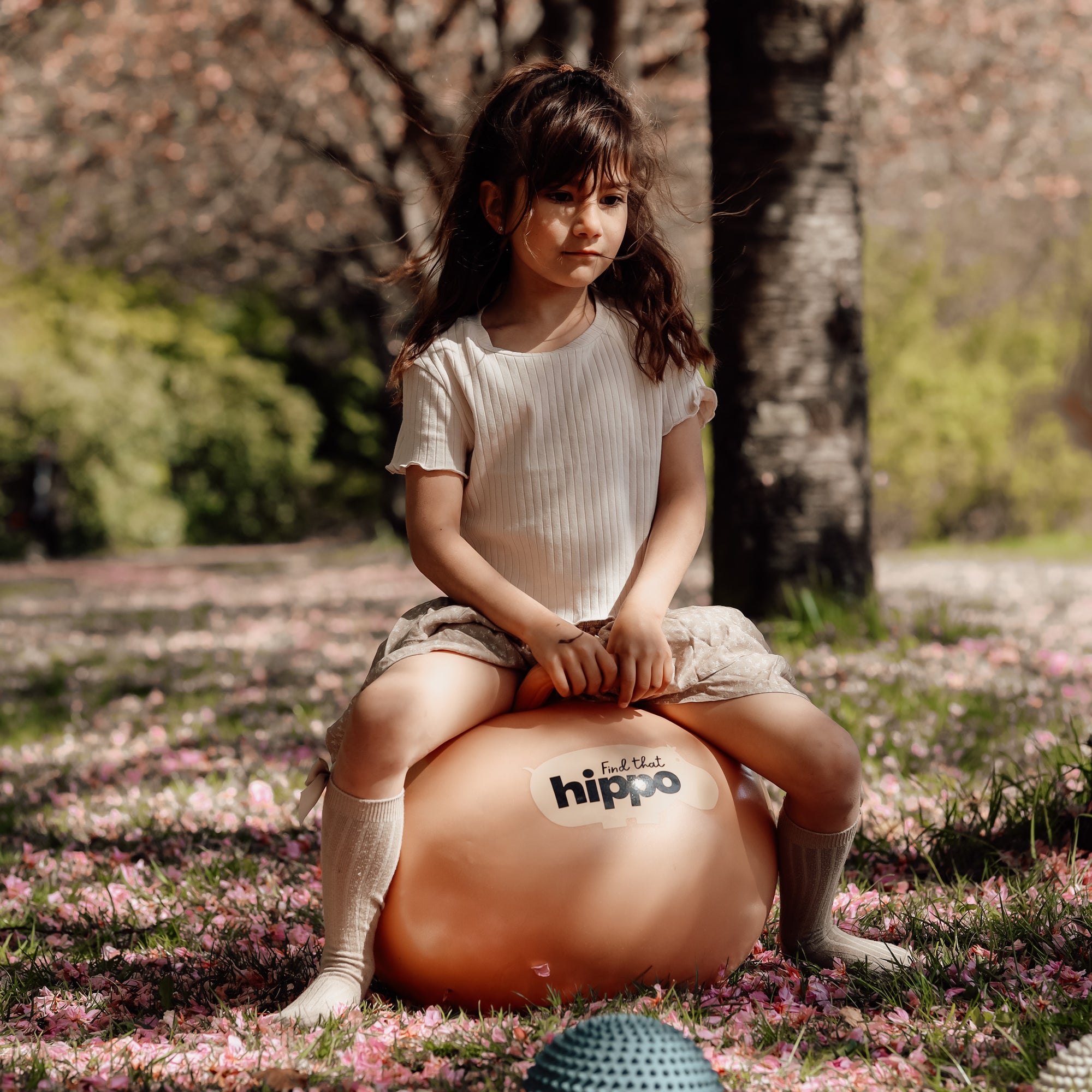 Child holding the handles of the muted orange bouncing ball outdoors – Find That Hippo