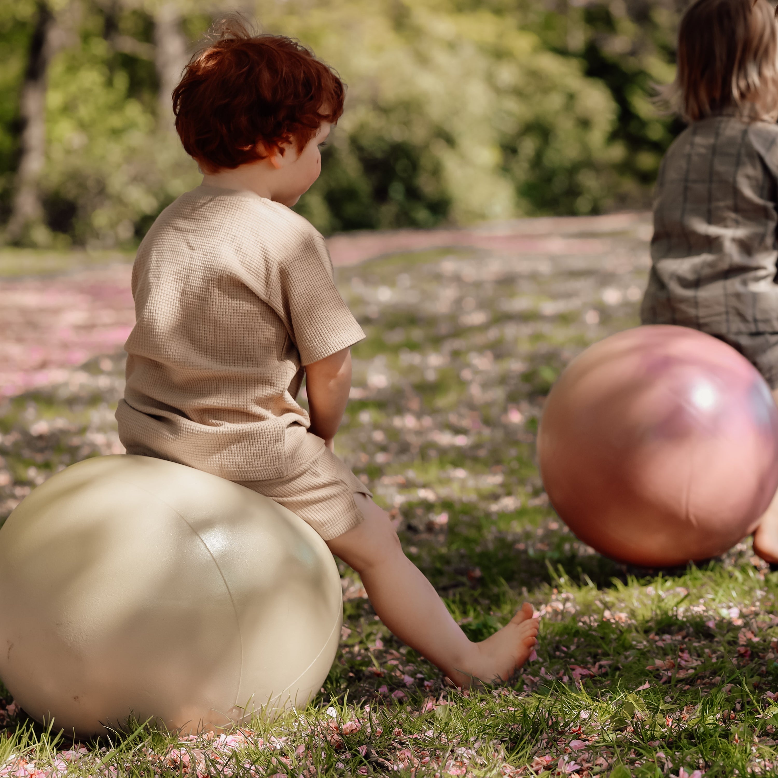 Two children playing outdoors with olive gold and dusty pink jumping balls – Find That Hippo