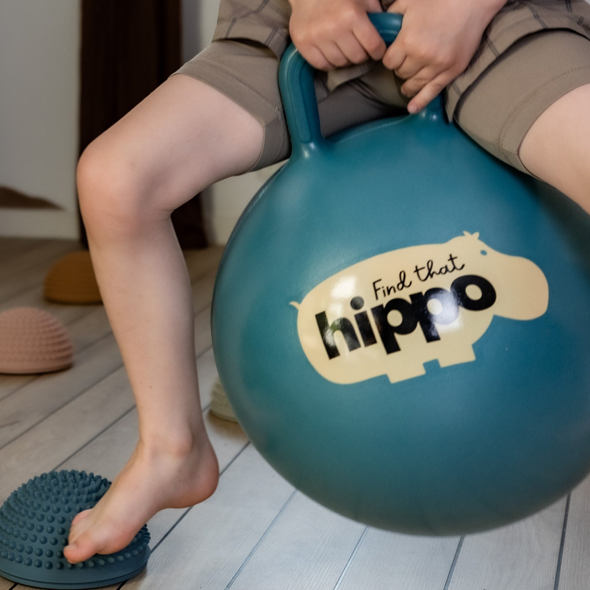 Close-up of child’s hands gripping the handle of petrol blue bouncing ball – Find That Hippo