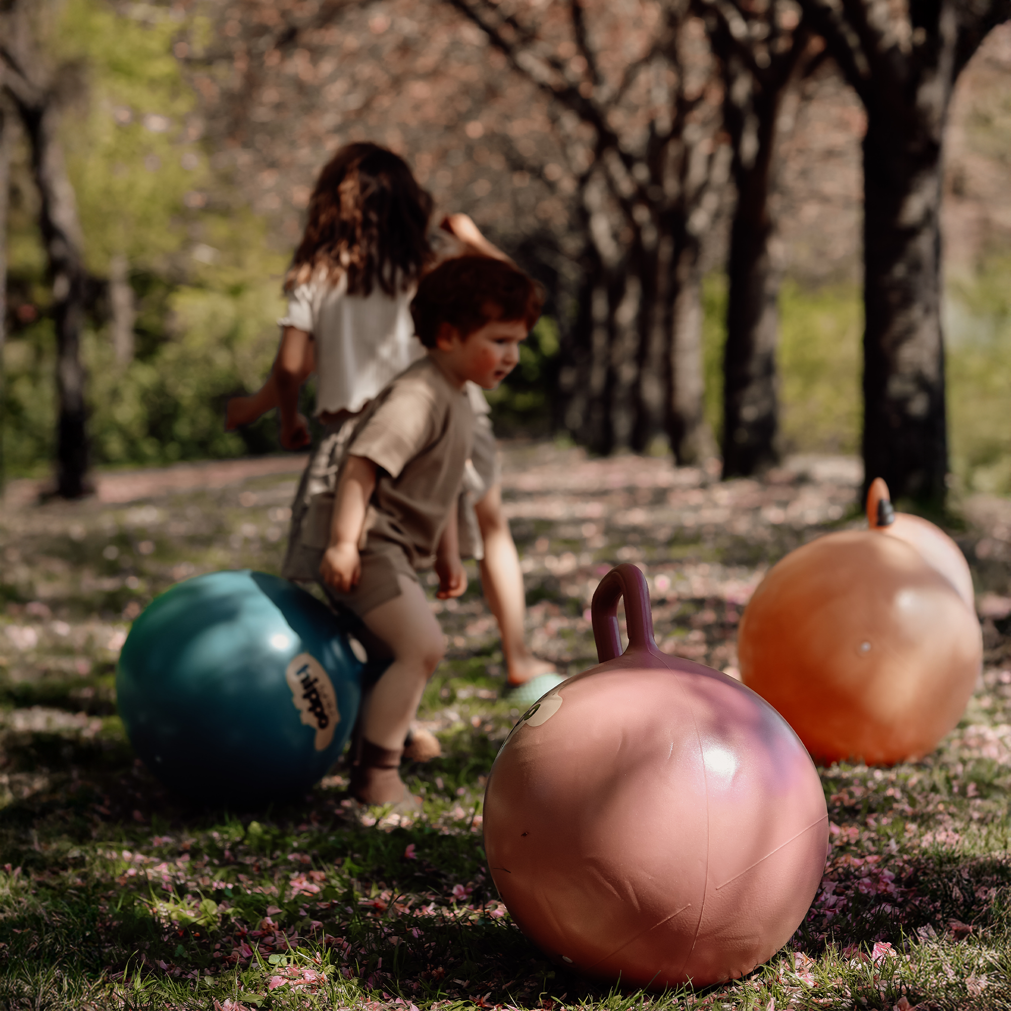 Two children playing on dusty pink and petrol blue Hippo hop balls under trees – Find That Hippo