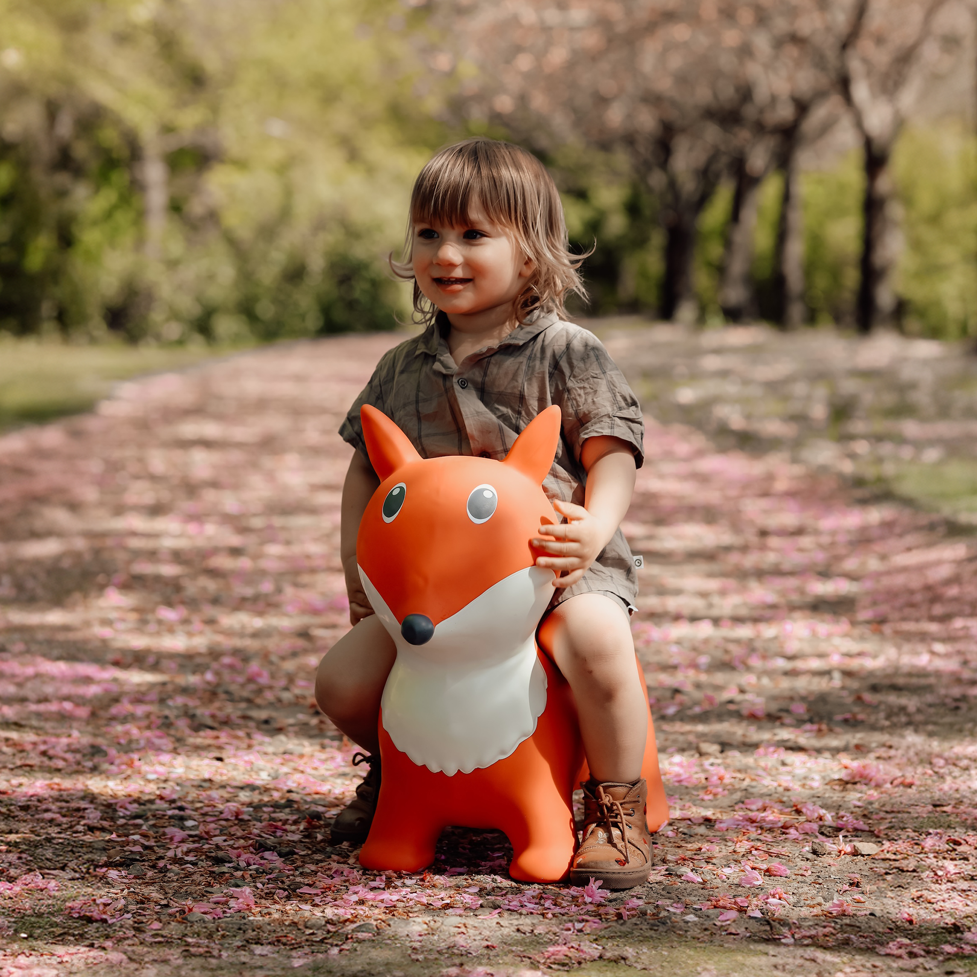 Child riding orange and white bouncing fox toy Lela on a pink flower-covered path – Find That Hippo