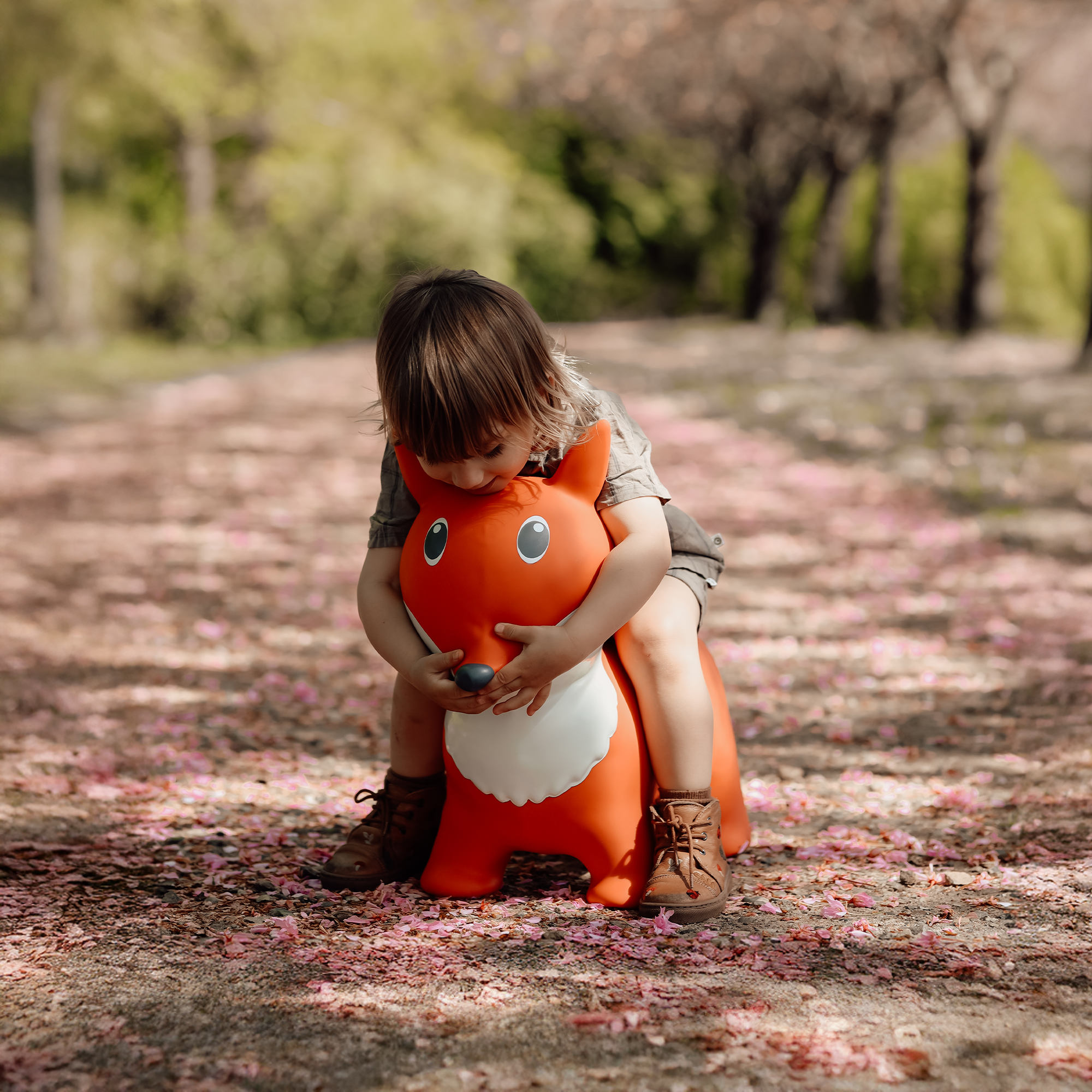 Child hugging orange and white bouncing fox toy Lela on a pink flower-covered path – Find That Hippo