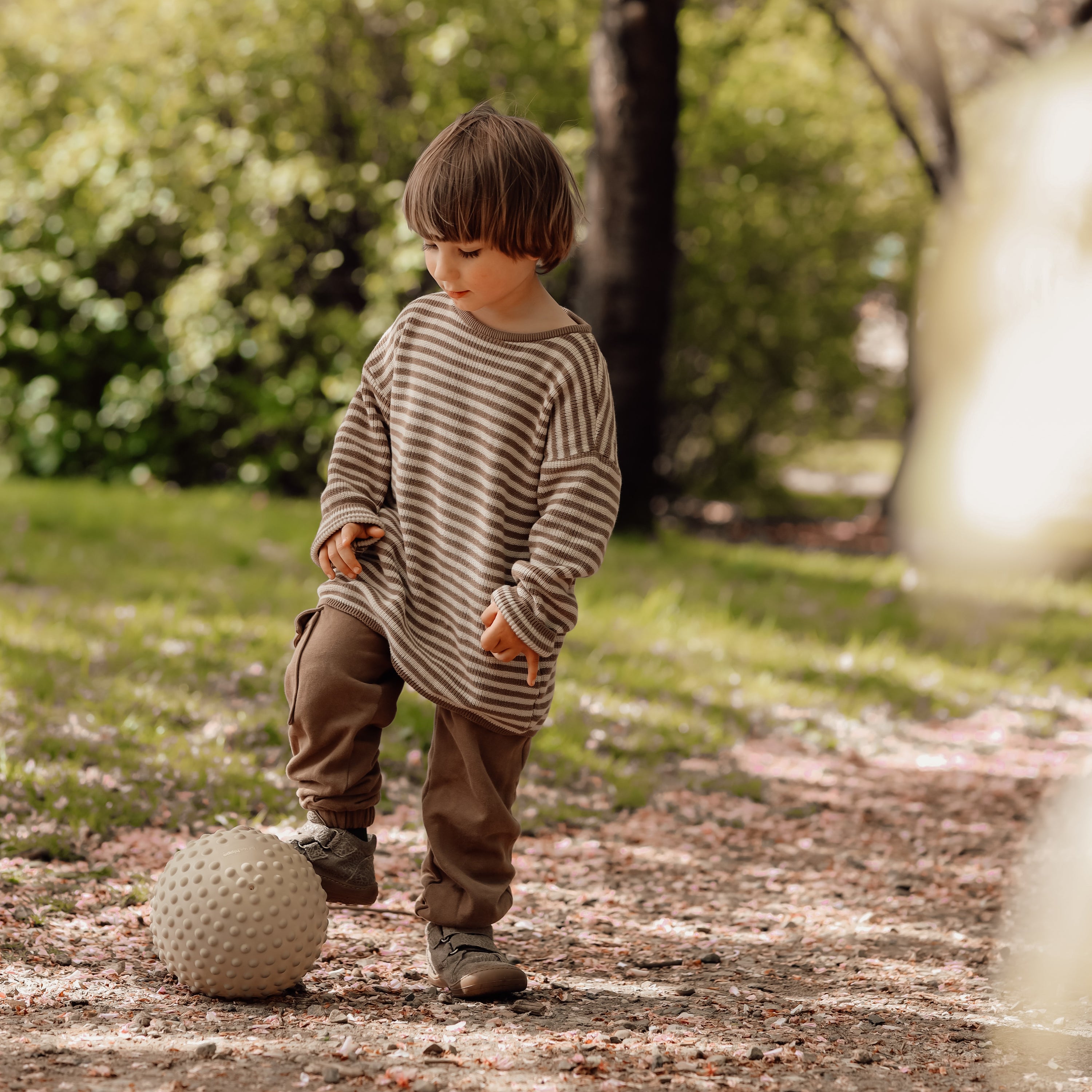 Child about to throw a large dusty green sensory ball in an outdoor park – Find That Hippo