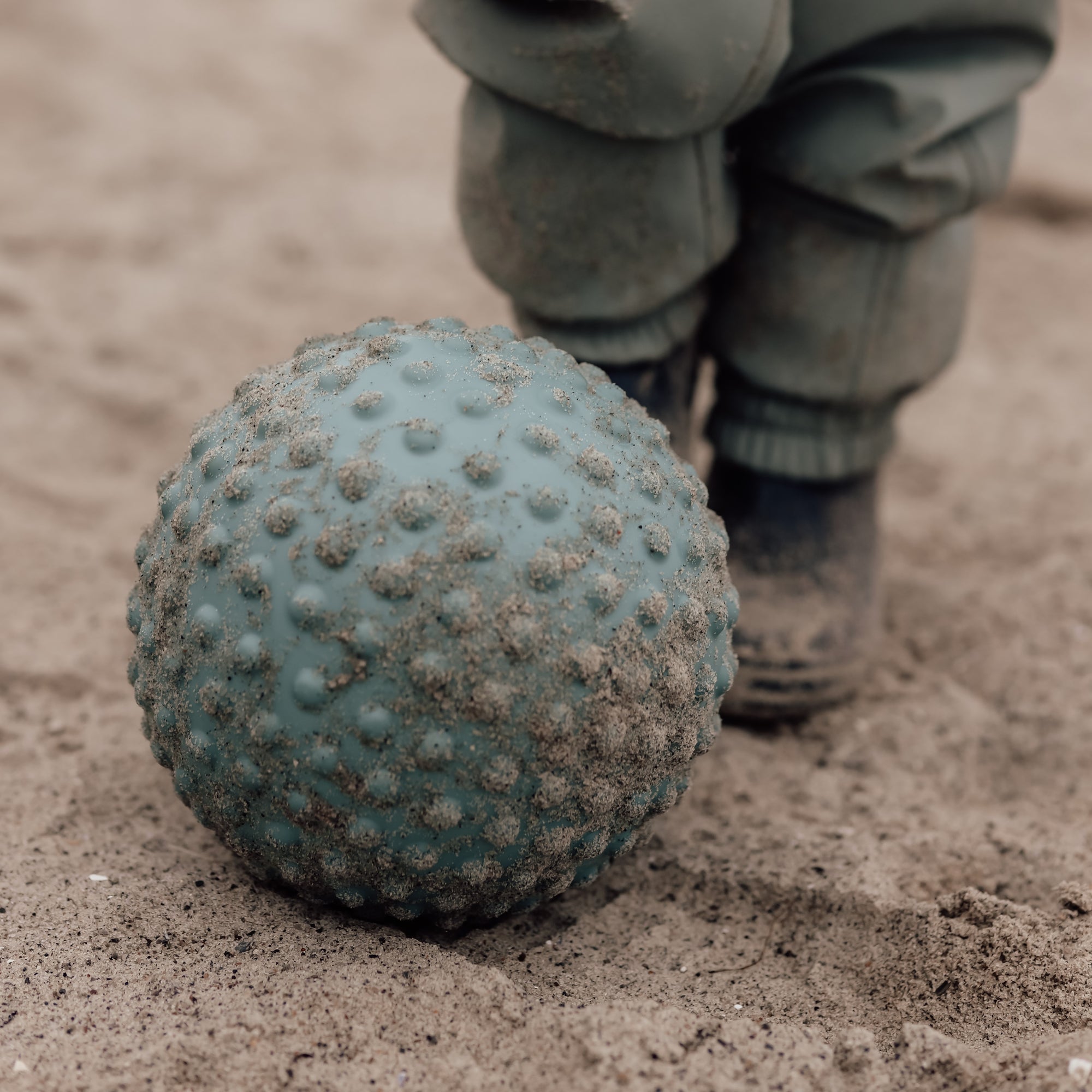 Close-up of a petrol blue sensory ball on beach with child’s boots in frame – Find That Hippo