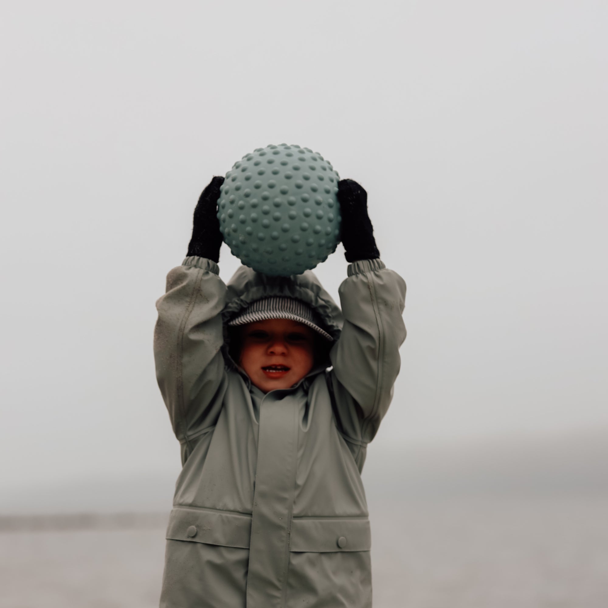 hild in green outfit holding petrol blue sensory ball in front of face – Find That Hippo