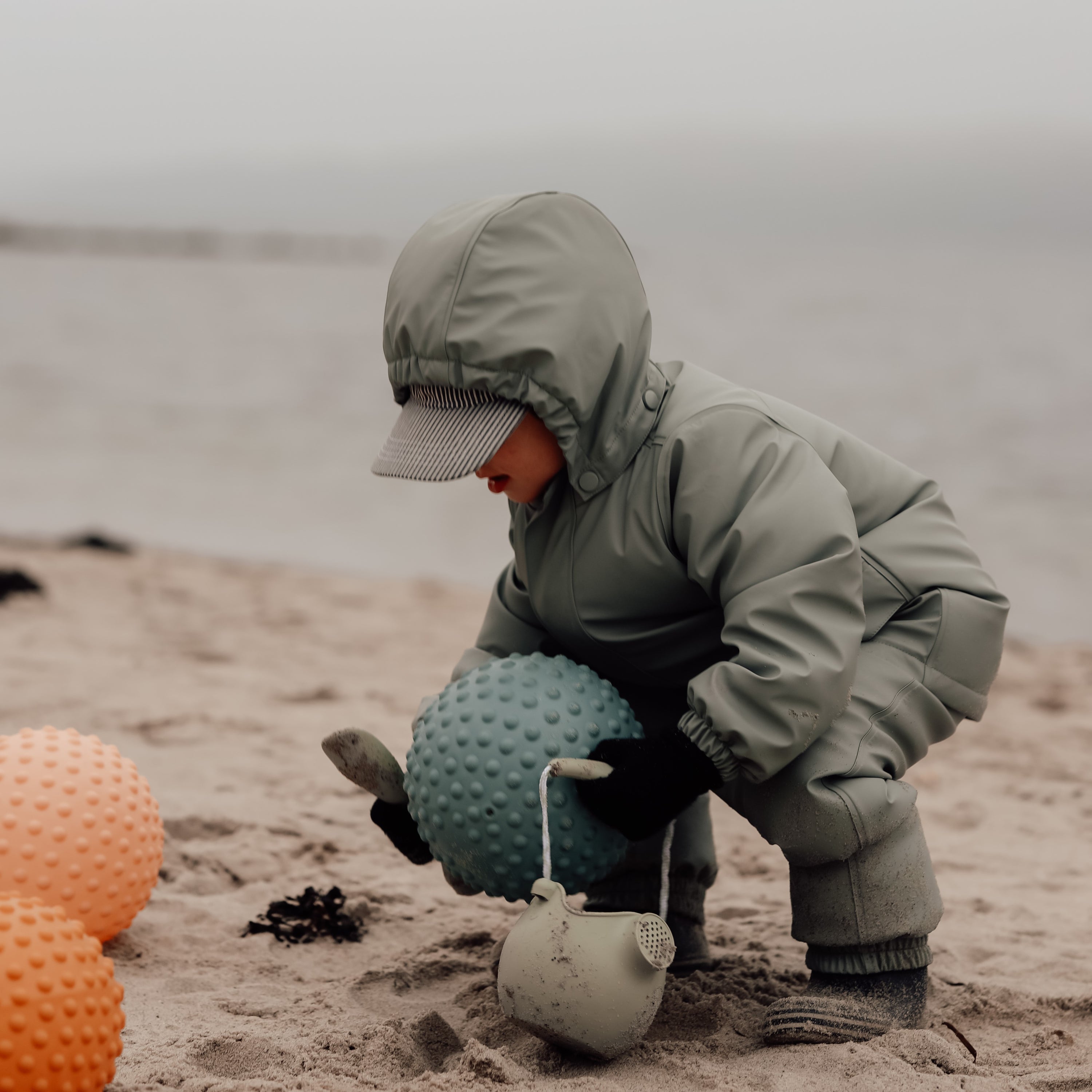Child crouching in sand while playing with a petrol blue sensory ball – Find That Hippo