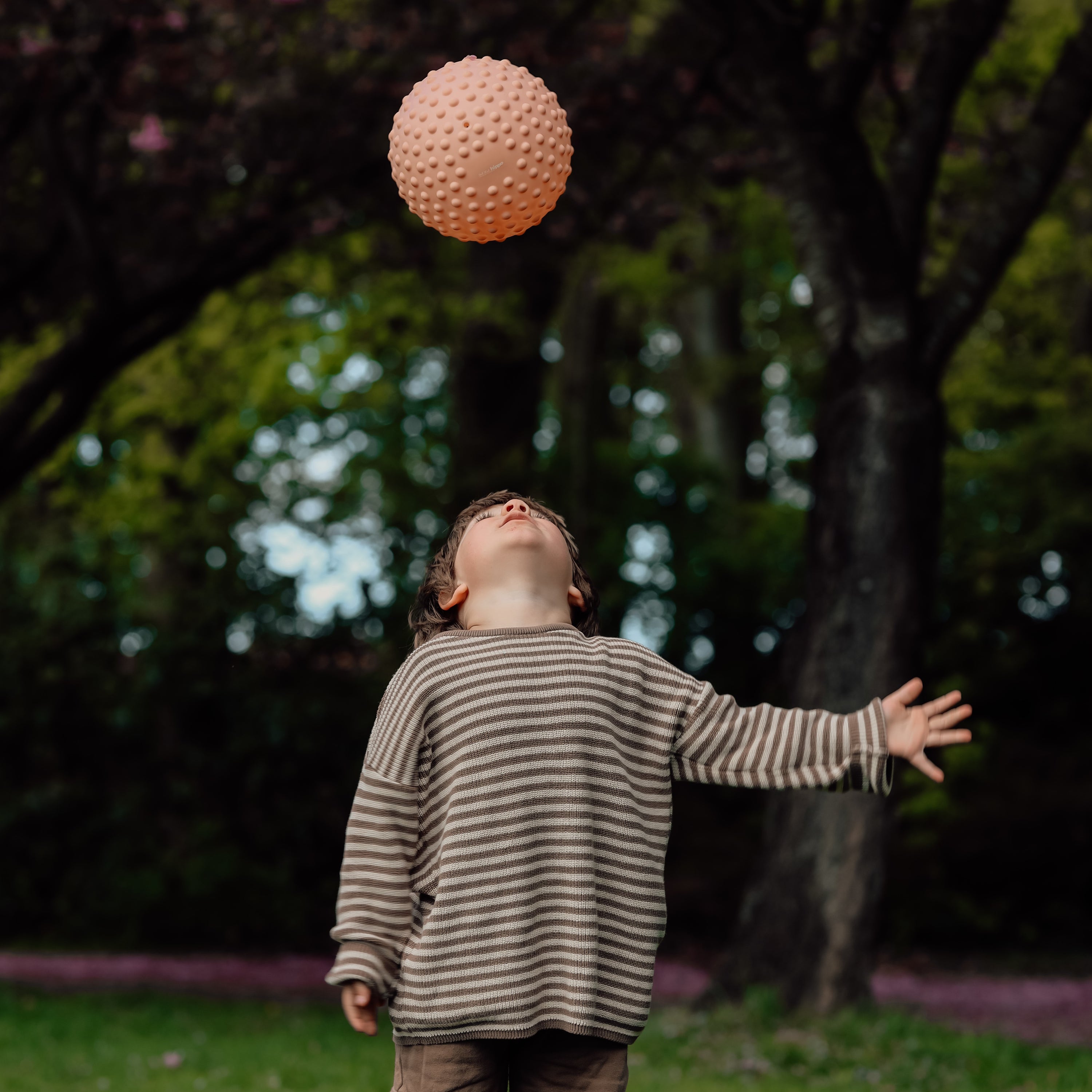 Child in striped shirt playing with a large pink sensory ball in the air outdoors – Find That Hippo