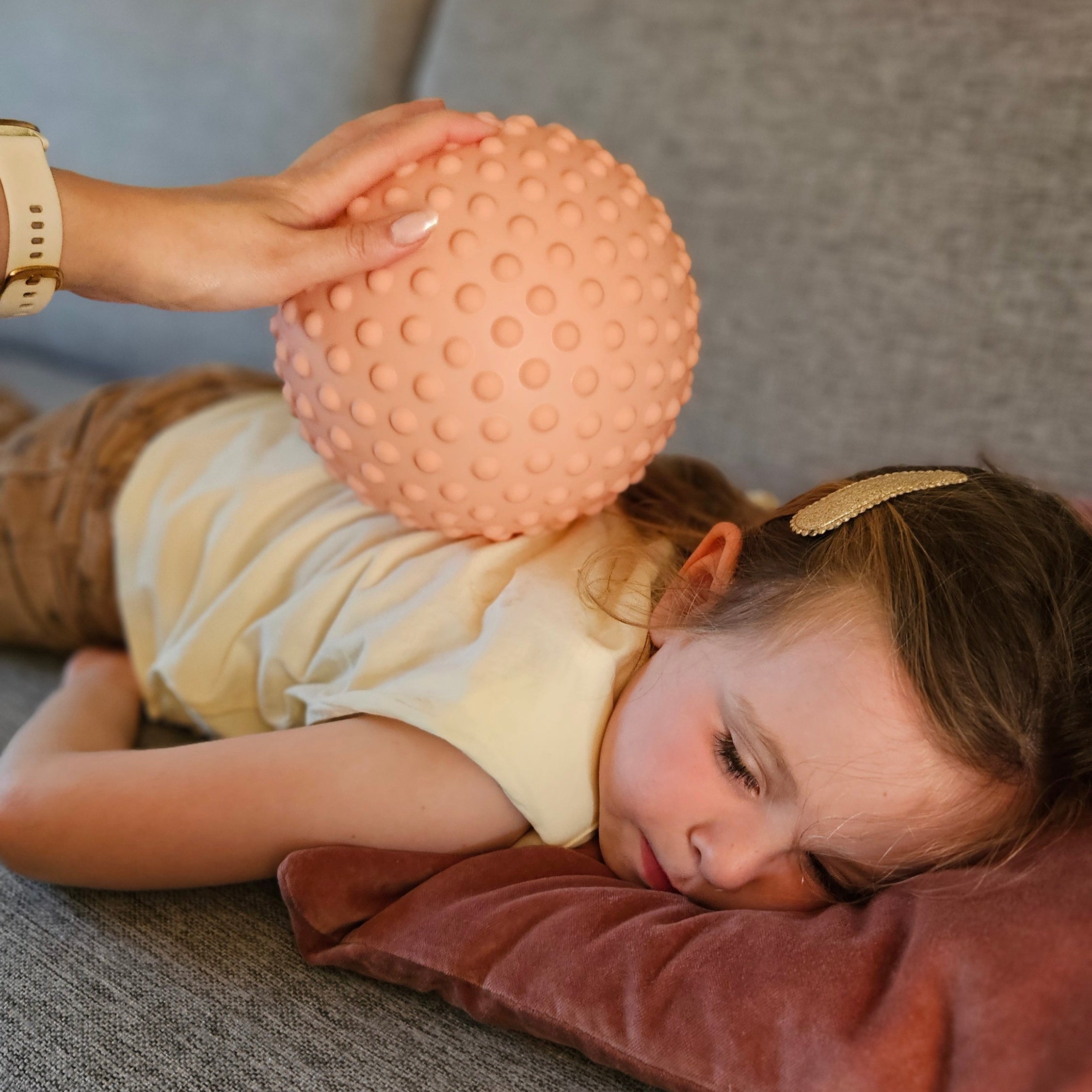 Child receiving a relaxing back massage with a dusty pink sensory ball.