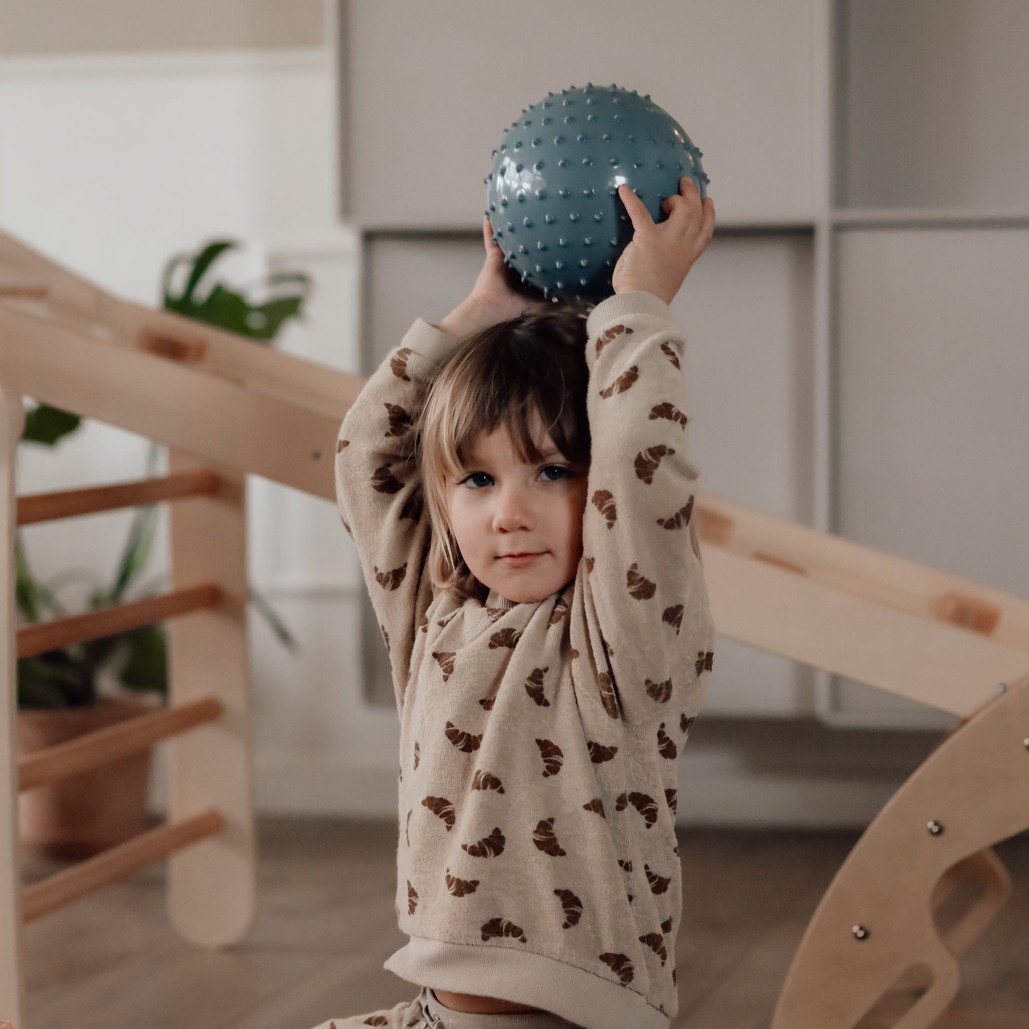 Child in dotted shirt balancing a blue-colored sensory ball on their head – Find That Hippo