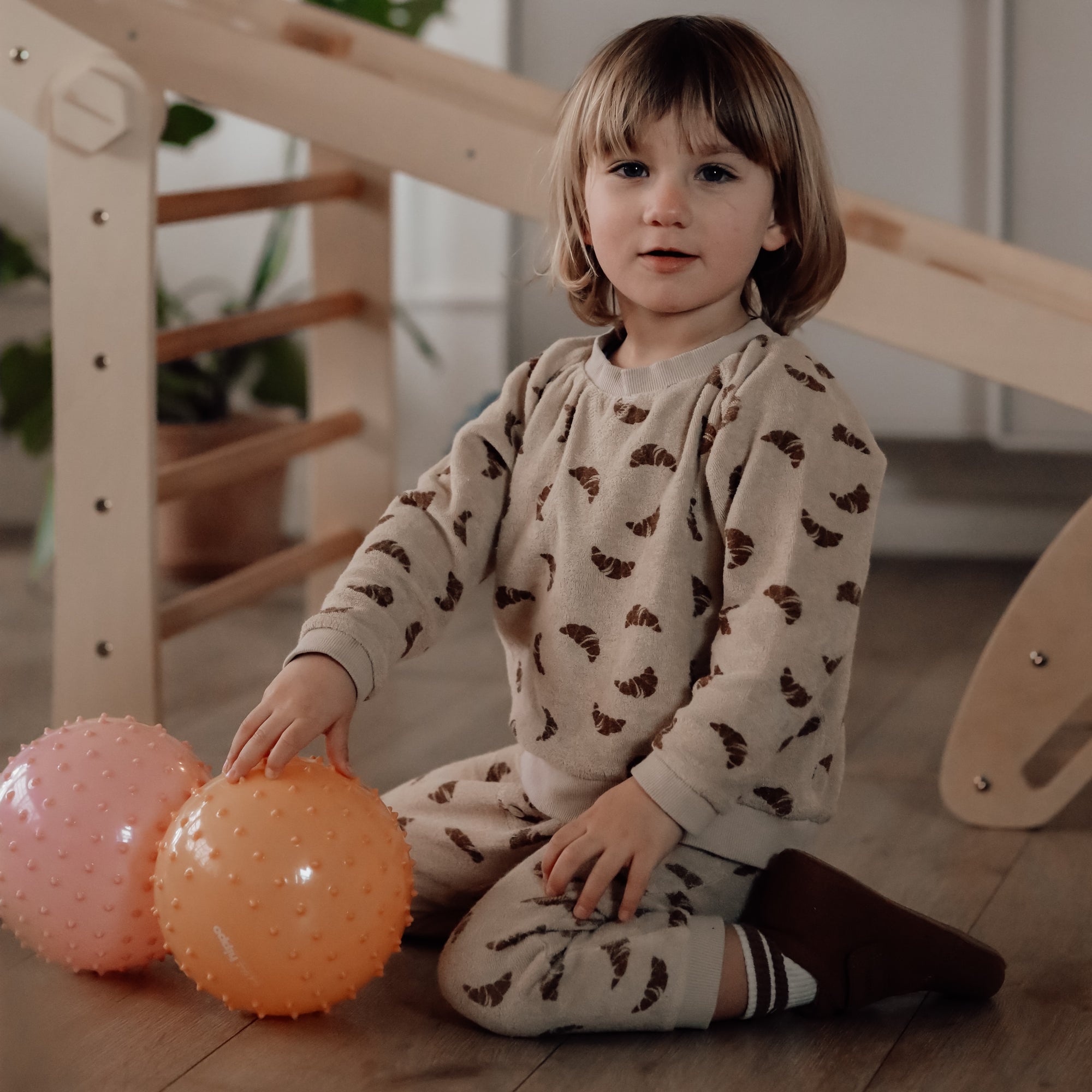 Young child sitting on the floor holding both dusty pink and muted orange sensory balls – Find That Hippo