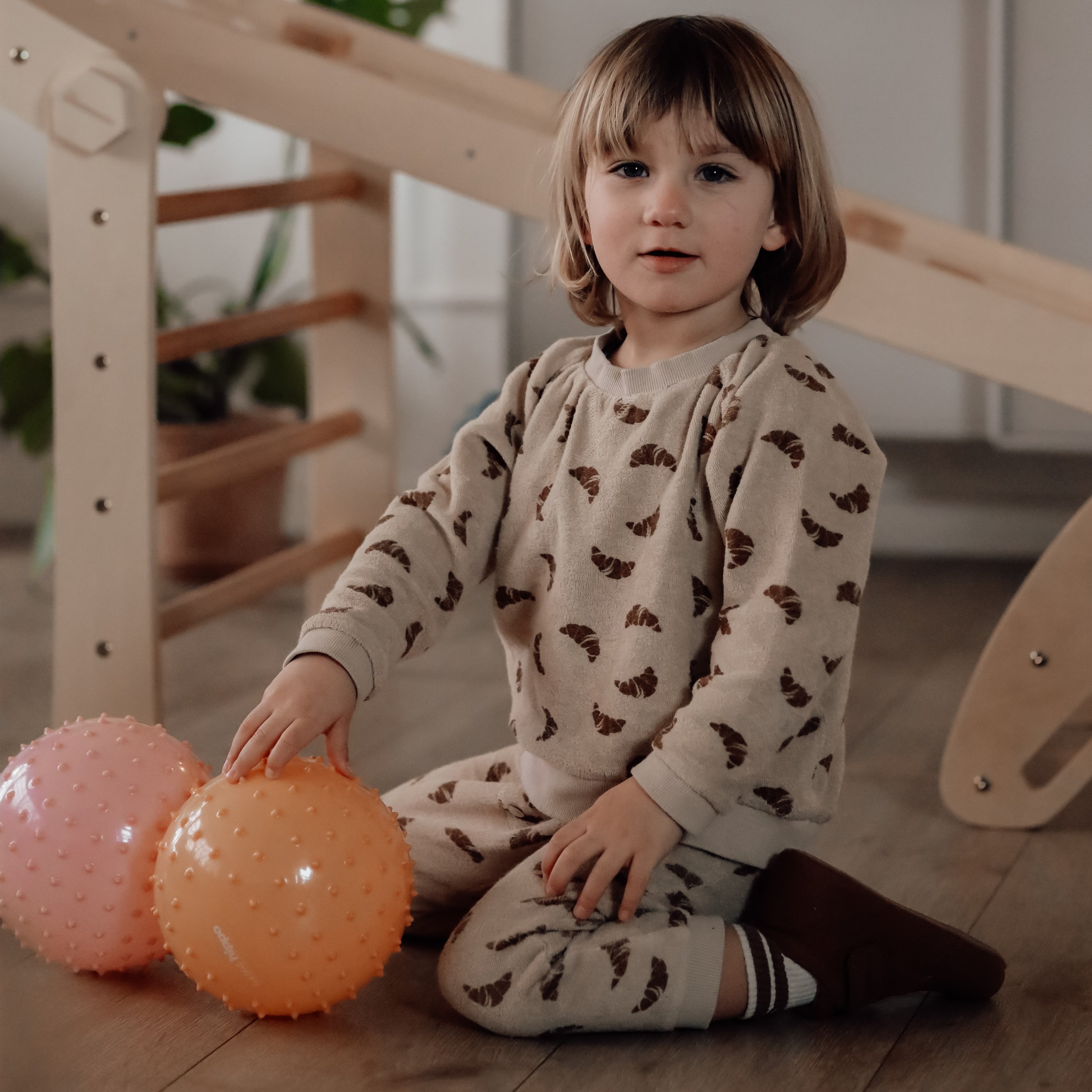 Young child sitting on the floor holding both dusty pink and muted orange sensory balls – Find That Hippo