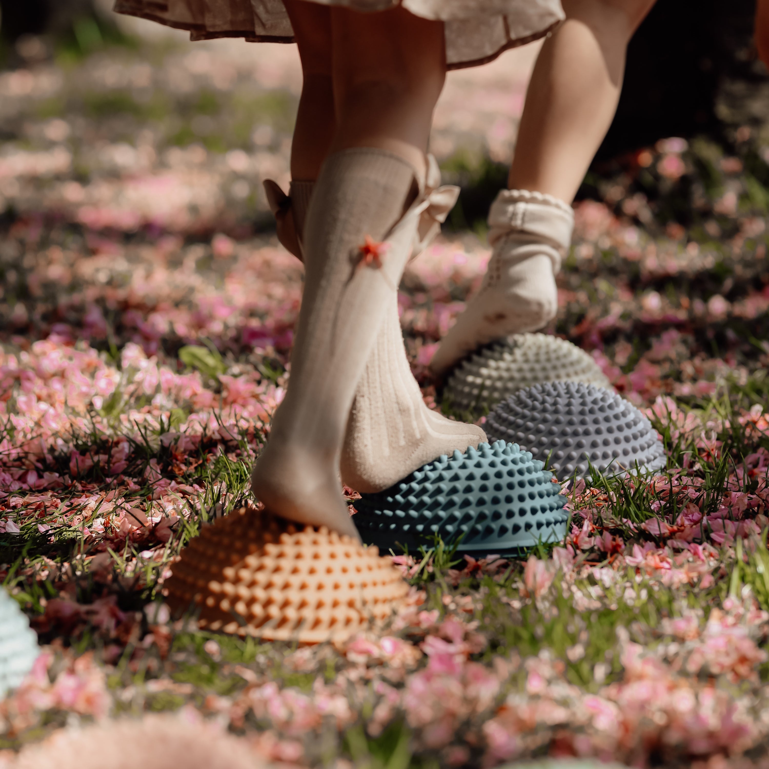 Child balancing on petrol-colored sensory stone with tactile knobs in a blooming outdoor field – Find That Hippo